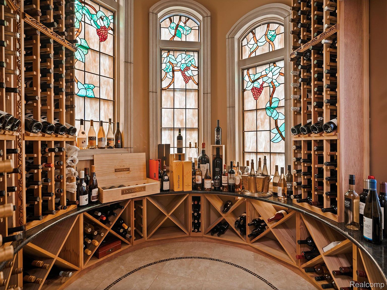 This is a well-stocked wine cellar featuring custom wooden racks that curve around a set of stained-glass windows. The racks are filled with various wine bottles, and the room has a tiled floor. The overall impression is one of luxury and sophistication, perfect for a wine enthusiast.