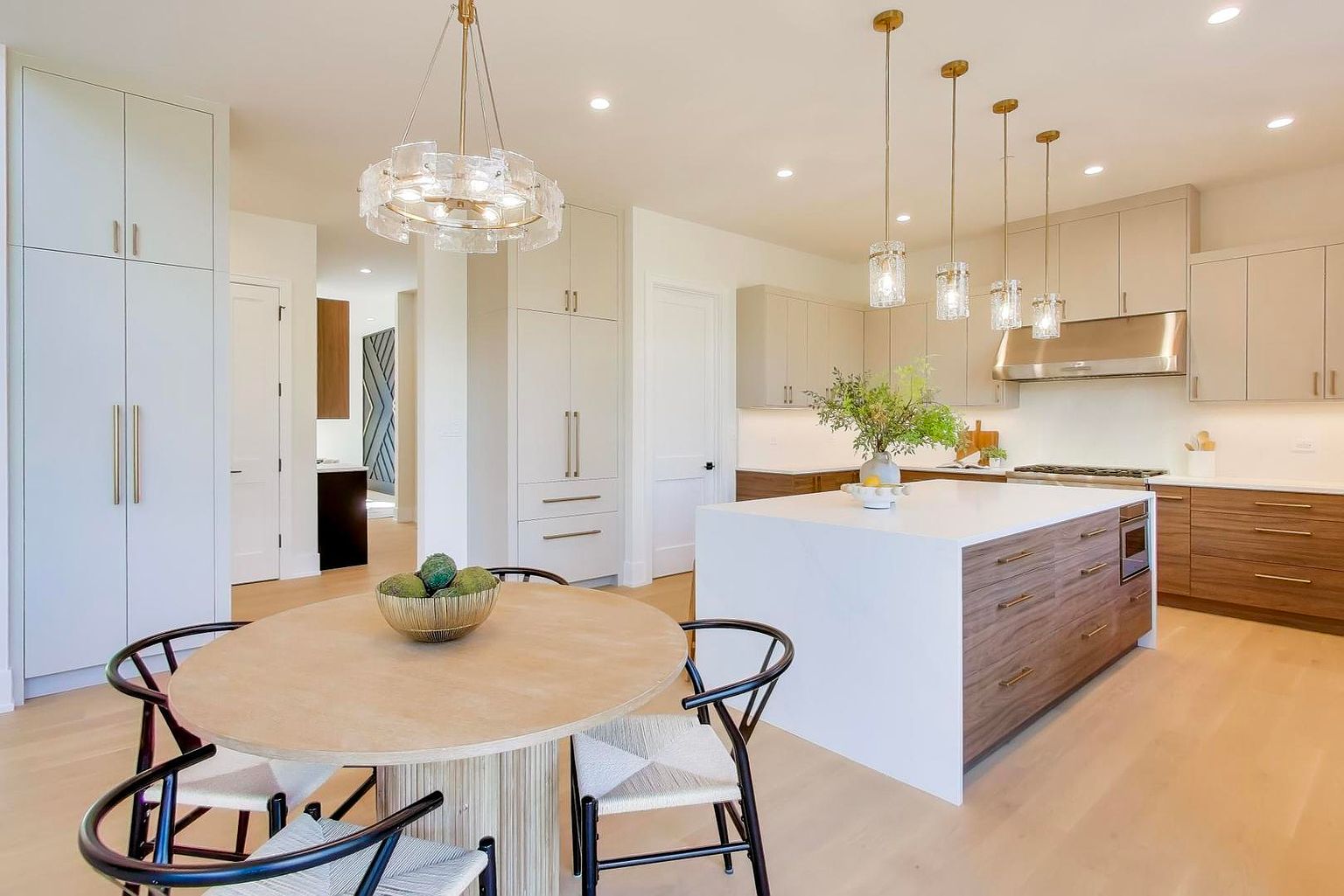 This is a bright and modern kitchen featuring two-tone cabinetry, a large island with a white countertop, and pendant lighting. The kitchen also has a round dining table with modern chairs. The overall impression is clean, stylish, and inviting, perfect for both cooking and entertaining.