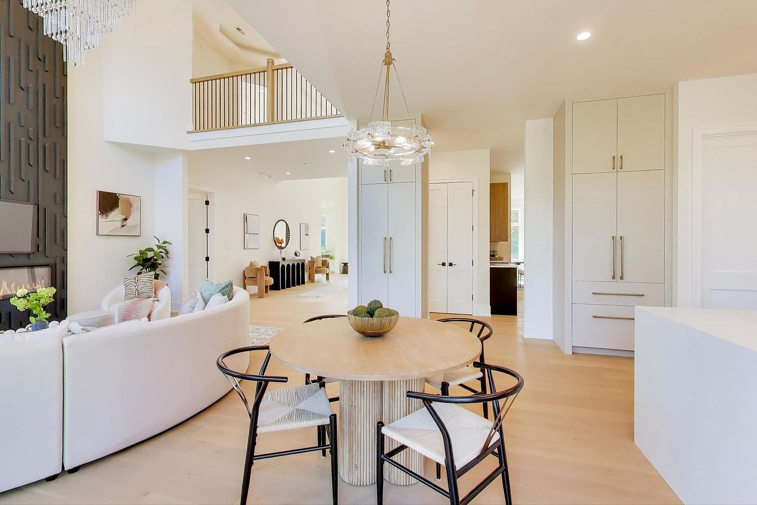 This interior shot showcases a bright and airy dining area with a round wooden table and modern chairs. The space features high ceilings, light wood floors, and a contemporary chandelier, creating an elegant and inviting atmosphere. The open floor plan seamlessly connects the dining area to the living room and kitchen, enhancing the sense of spaciousness.