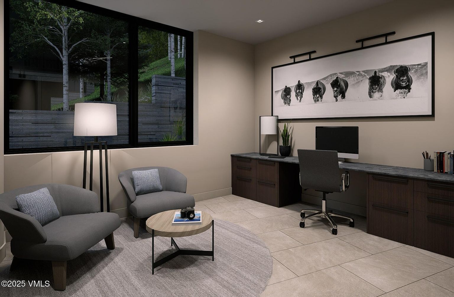 This is an interior shot of a modern office space. The room features a long desk with dark wood cabinetry, a gray office chair, and a large black and white photograph above the desk. A seating area with two gray armchairs and a round coffee table is situated near a large window, creating a comfortable and functional workspace.