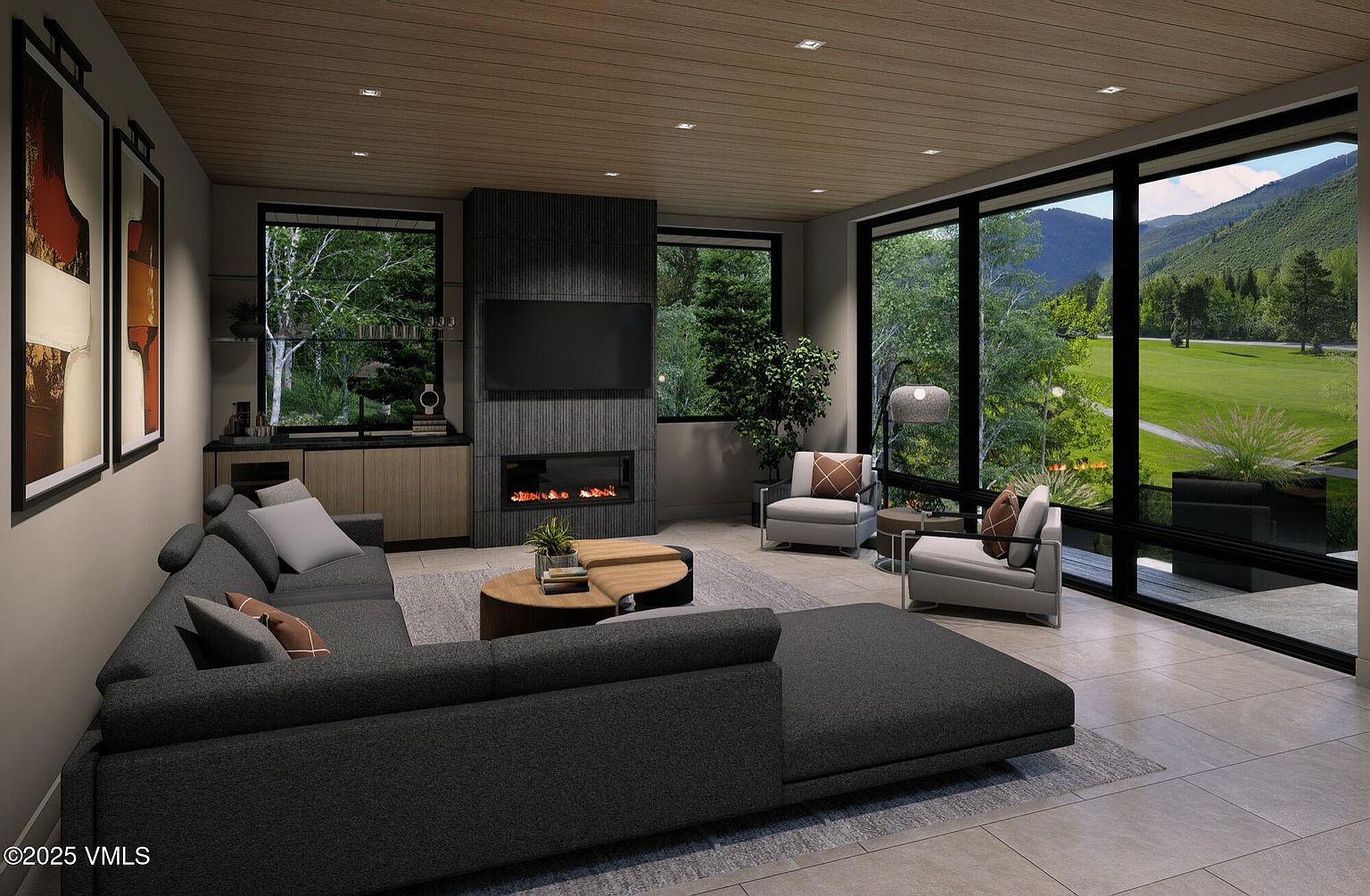 This is a modern living room featuring a large sectional sofa, a fireplace with a mounted TV above, and floor-to-ceiling windows offering a view of a lush green landscape. The room is decorated in neutral tones with wood accents on the ceiling and cabinetry, creating a warm and inviting atmosphere. The overall impression is one of luxury and comfort.
