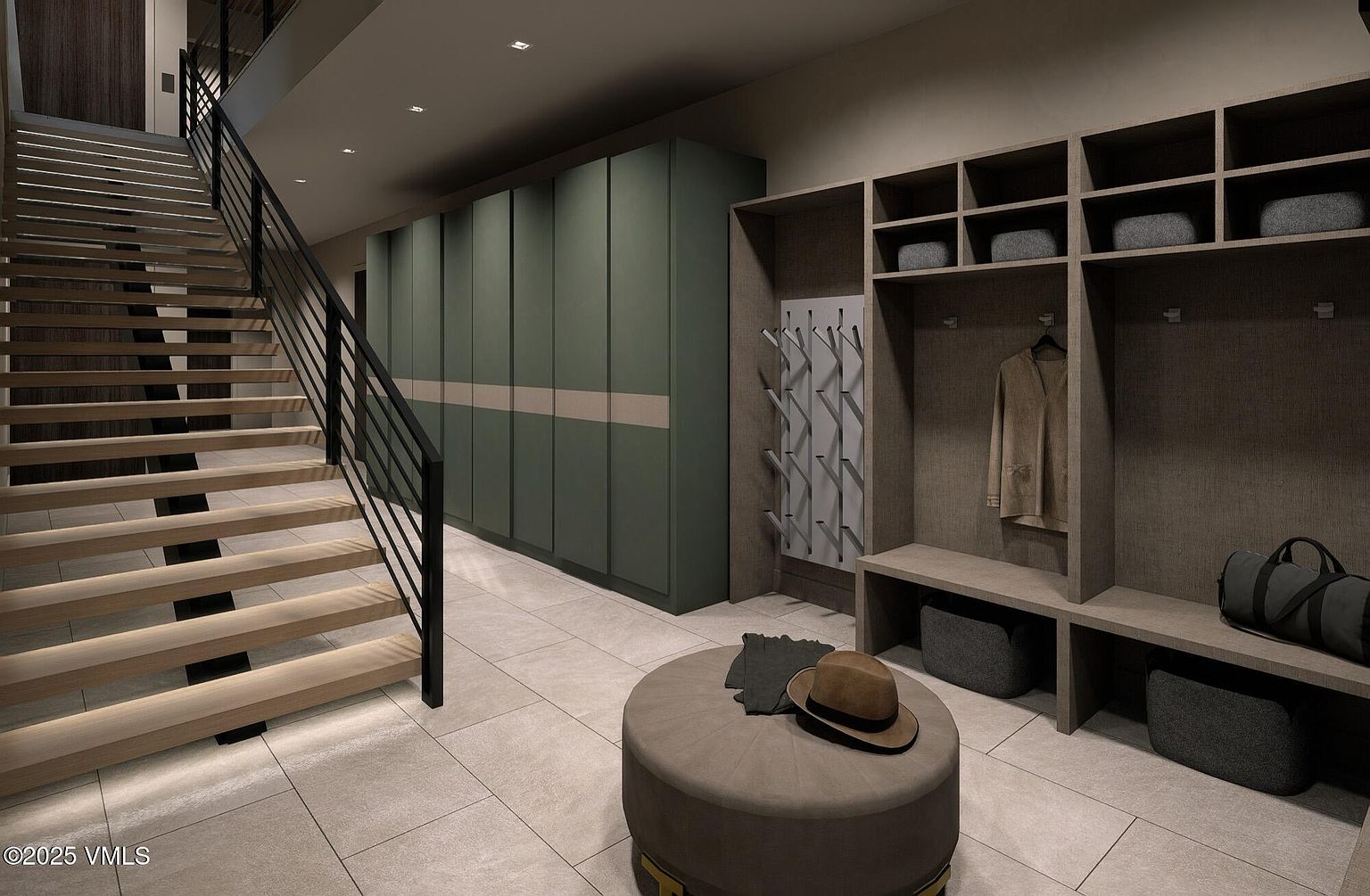 This interior shot showcases a modern hallway with a staircase and built-in storage. The staircase features open treads and a dark metal railing, while the hallway includes green storage cabinets and a custom shelving unit with cubbies and hooks. An ottoman with a hat and gloves sits in the foreground, adding a touch of personal style to the space.