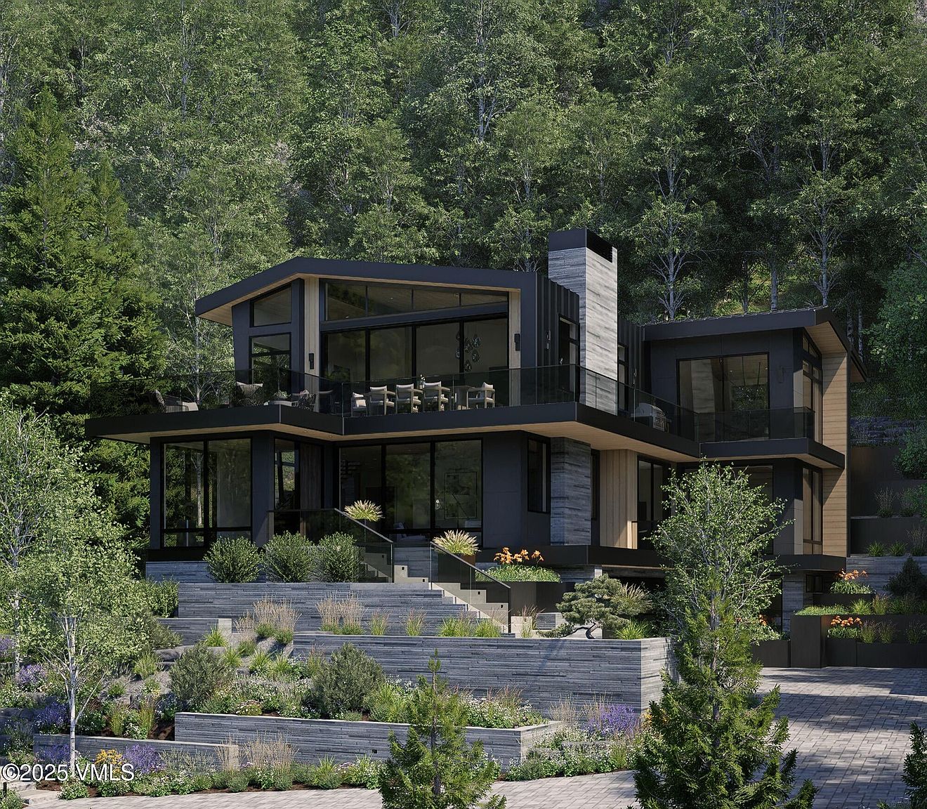 This is a stunning front view of a modern, multi-level home nestled in a lush, wooded setting. The house features clean lines, large windows, and a combination of dark siding and natural wood accents. The landscaping is meticulously designed with tiered garden beds and stone retaining walls, creating an inviting and sophisticated curb appeal.