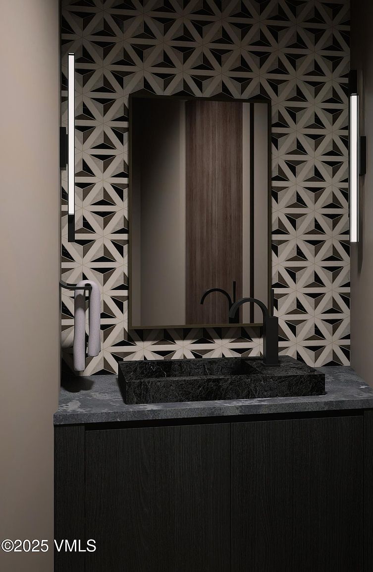 This is a detailed shot of a modern bathroom vanity. The vanity features a dark wood cabinet, a dark stone countertop with a rectangular vessel sink, and a black faucet. A mirror hangs above the sink, flanked by vertical light fixtures, and the wall is covered in a geometric patterned tile. The perspective is a medium shot, focusing on the vanity area.