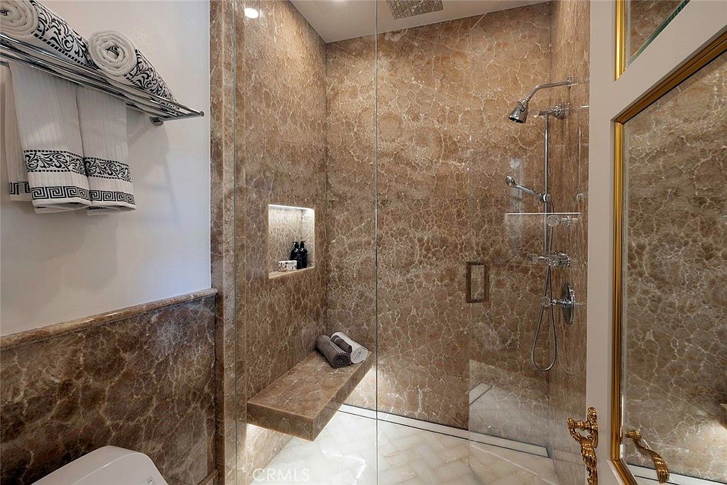 This is a luxurious primary bathroom featuring marble walls and flooring, a glass-enclosed shower with a built-in bench and niche for toiletries, and a high-end shower system. The design exudes elegance and sophistication, creating a spa-like atmosphere. The perspective is from the entrance of the shower.