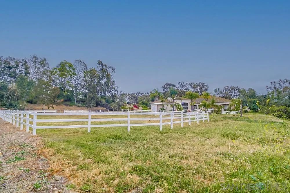 This exterior shot showcases a sprawling yard with lush green grass and a white fence that encloses the property. In the background, a well-maintained house is visible, surrounded by mature trees and landscaping. The overall impression is one of spaciousness and tranquility, ideal for outdoor activities and relaxation.