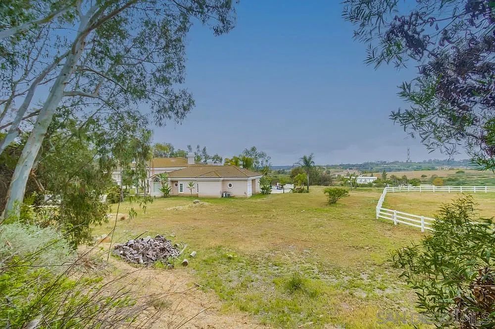 This image showcases a sprawling yard with a well-maintained lawn and a charming house in the background. A white fence adds a touch of elegance and defines the property line. The scene evokes a sense of tranquility and spaciousness, highlighting the property's outdoor appeal.