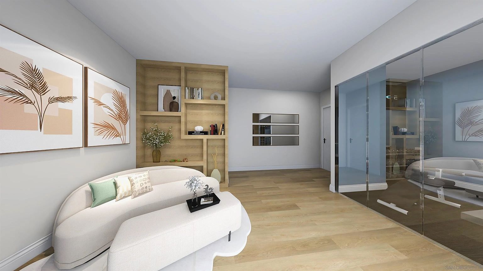 This is an interior shot of a modern living room featuring a curved white sofa with decorative pillows and a matching ottoman. The room is decorated with abstract art and a built-in wooden bookshelf. The flooring is light wood, and there is a glass-enclosed area that appears to be a wine cellar or additional living space.