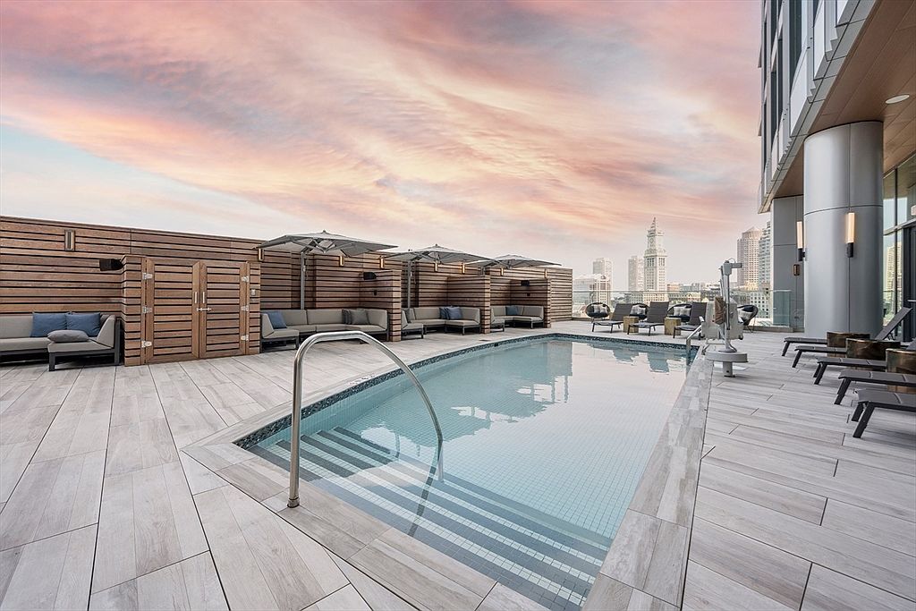 This image showcases a luxurious rooftop pool area, complete with lounge chairs, shaded cabanas, and a stunning city skyline backdrop. The pool's clear water and modern design create an inviting and upscale atmosphere, perfect for relaxation and entertainment. The wooden decking and privacy walls add a touch of warmth and sophistication.