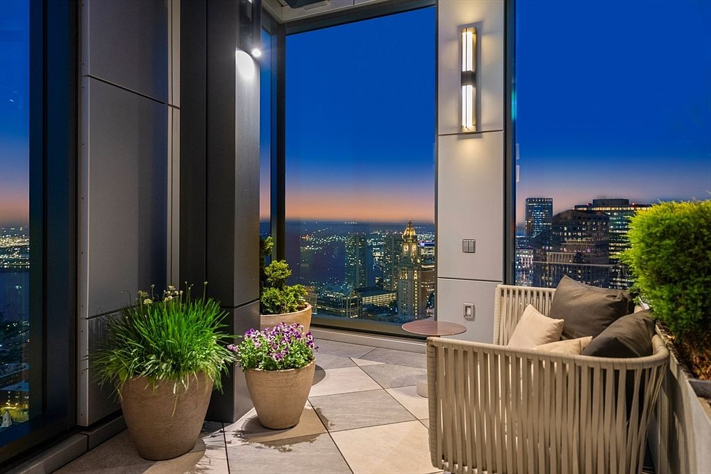 This image showcases a luxurious balcony with a stunning city view at dusk. The balcony features stylish outdoor furniture, including a woven chair with plush pillows, and potted plants adding a touch of greenery. The high-rise setting offers a breathtaking panorama of the cityscape, making it an ideal space for relaxation and entertainment.