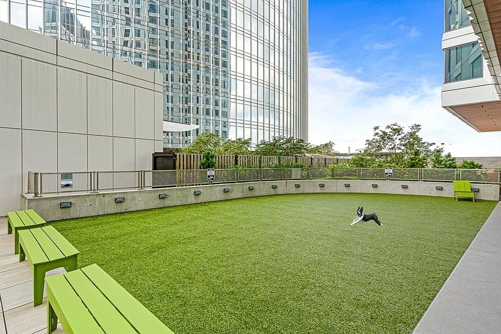 This image showcases a well-maintained dog park amenity within a residential community. The park features artificial turf, providing a clean and safe environment for pets to play. Green benches and a secure fence surround the area, offering a comfortable and secure space for residents and their dogs.