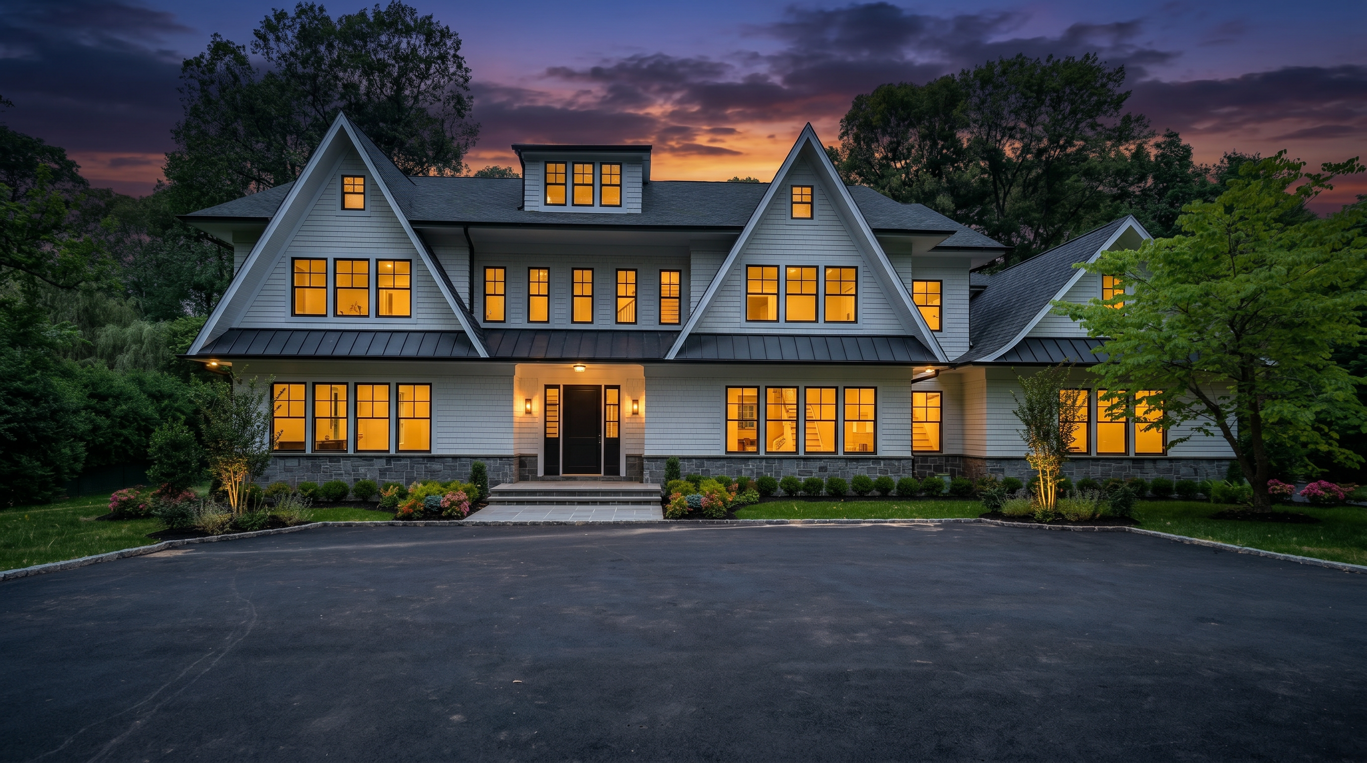 This is a stunning custom-built home featuring a classic, modern farmhouse design with white shiplap siding, dark-framed windows, and a dark metal roof. The symmetrical front facade is highlighted by warm interior lighting, a grand entryway, and meticulous landscaping, all set against a beautiful twilight sky. It offers exceptional curb appeal, characterized by high-end architectural details and a spacious, well-manicured driveway.