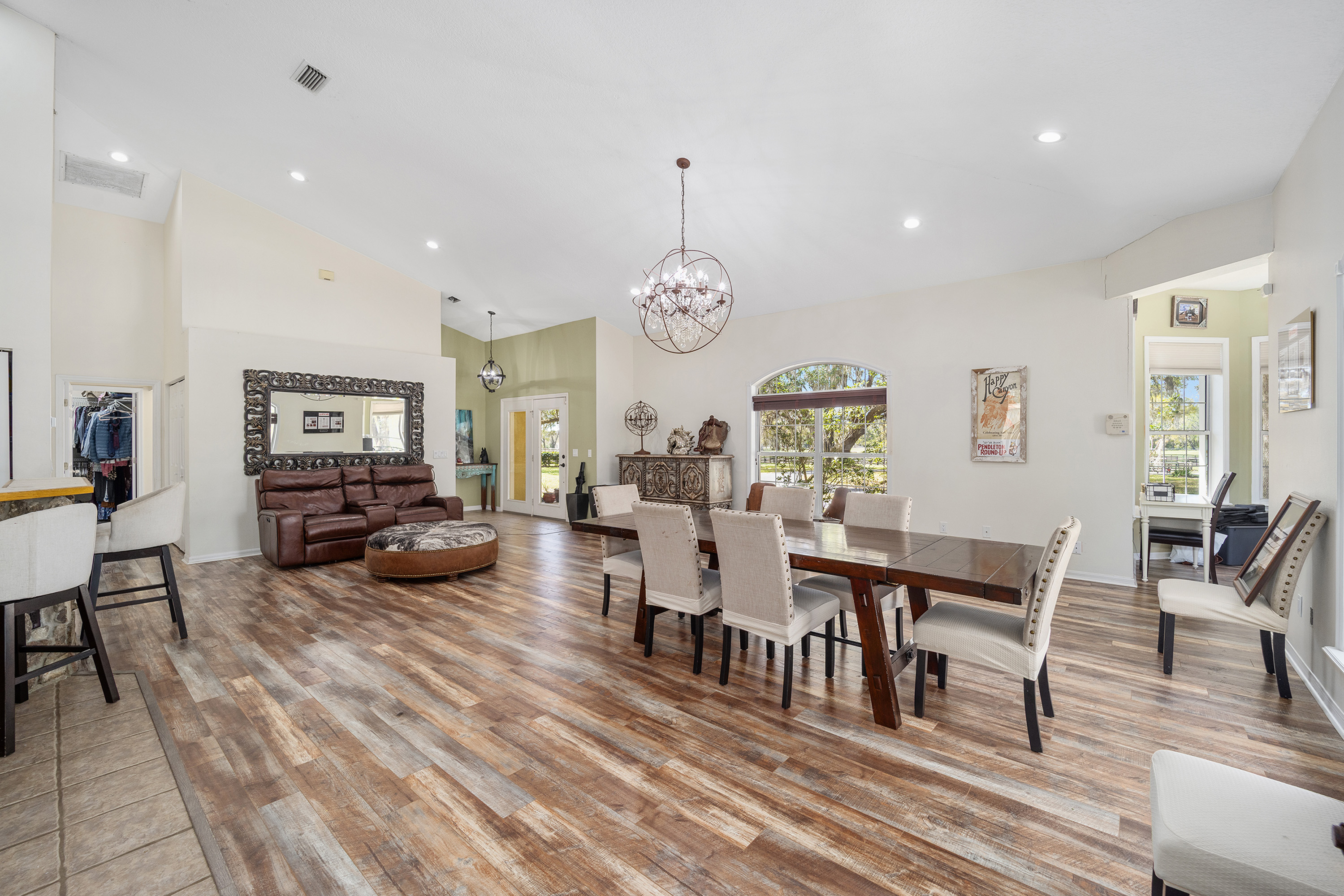 This is an interior shot of a dining room. The room features a large wooden dining table with upholstered chairs, accented by a chandelier. The hardwood flooring and ample natural light contribute to an inviting atmosphere, suitable for both casual meals and formal gatherings.