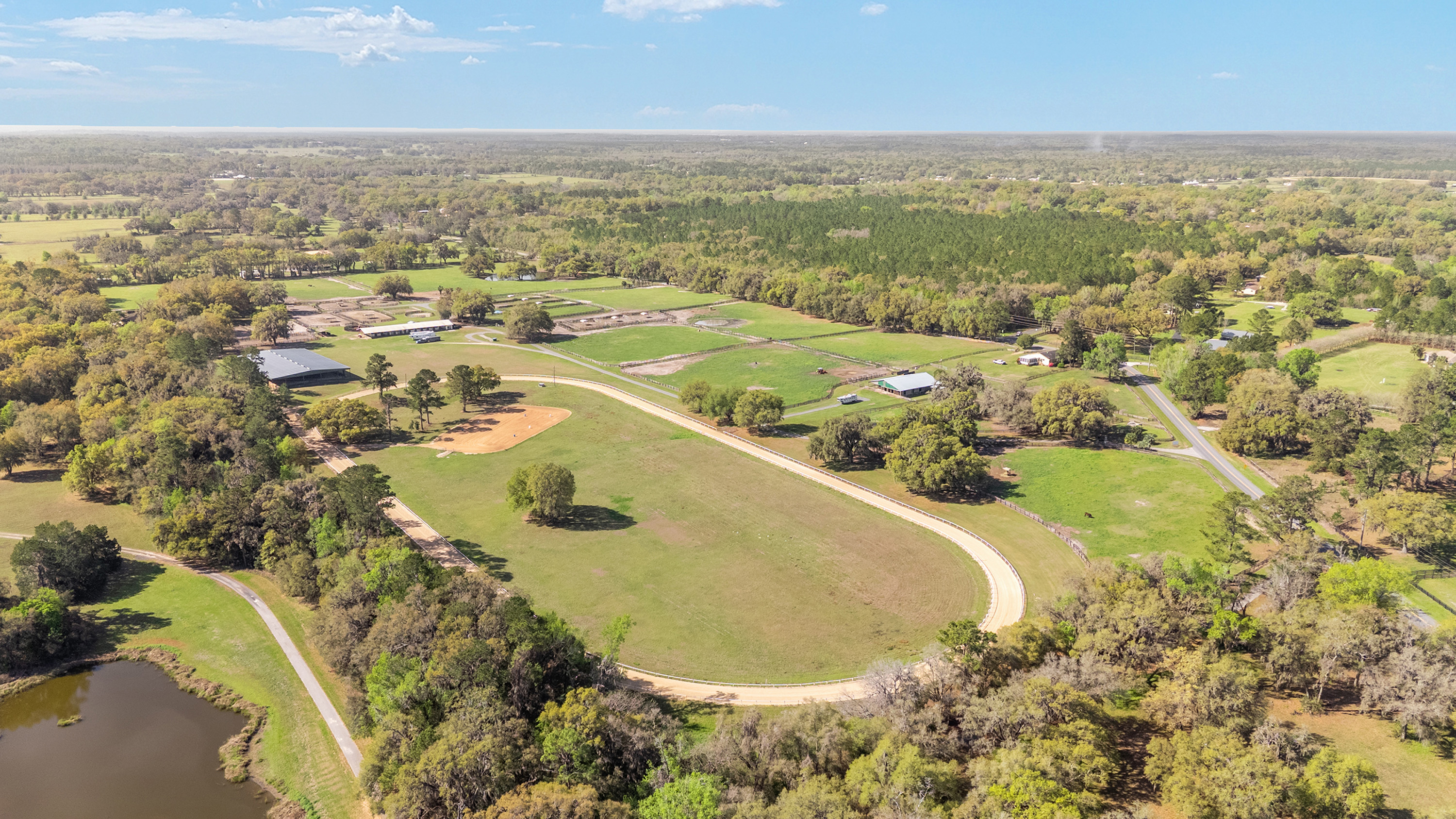 This aerial view showcases a sprawling equestrian estate. Manicured grounds include pastures, a racetrack, barns, and training facilities. Mature trees provide shade and enhance the property's privacy.