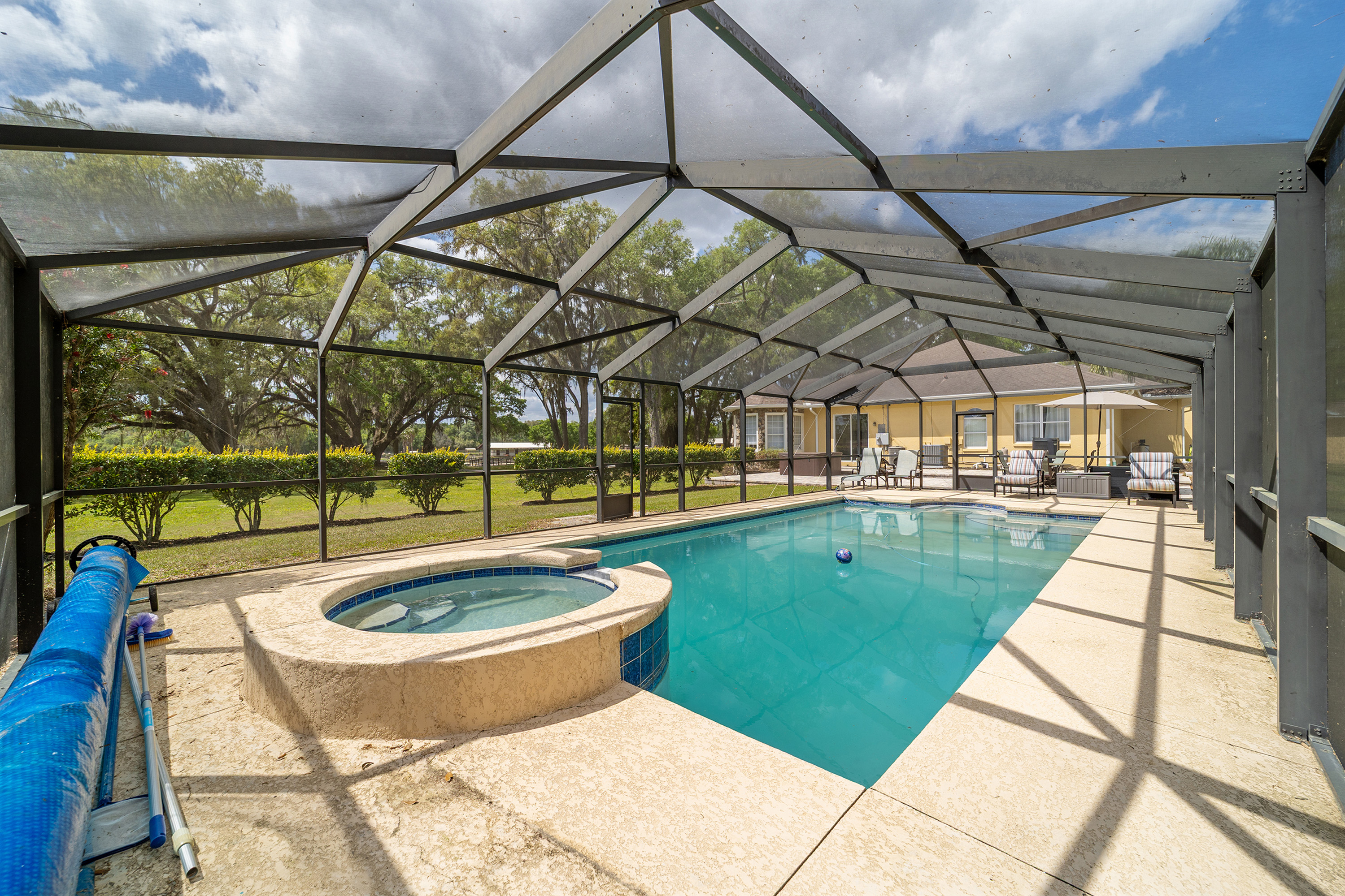 This image showcases a backyard pool and spa area enclosed within a screened-in enclosure. The pool features clear blue water and is adjacent to a raised spa with a tiled exterior. The enclosure protects the area from insects and debris, creating a comfortable and private outdoor living space.