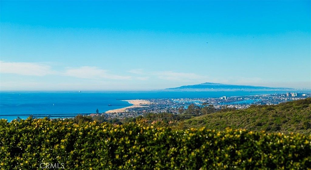 This aerial view showcases a stunning coastal landscape, featuring a sandy beach, a vibrant city, and a distant mountain range under a clear blue sky. Lush greenery in the foreground adds depth and frames the scene, creating a picturesque and desirable setting. The image highlights the proximity to both natural beauty and urban amenities, making it an attractive location.