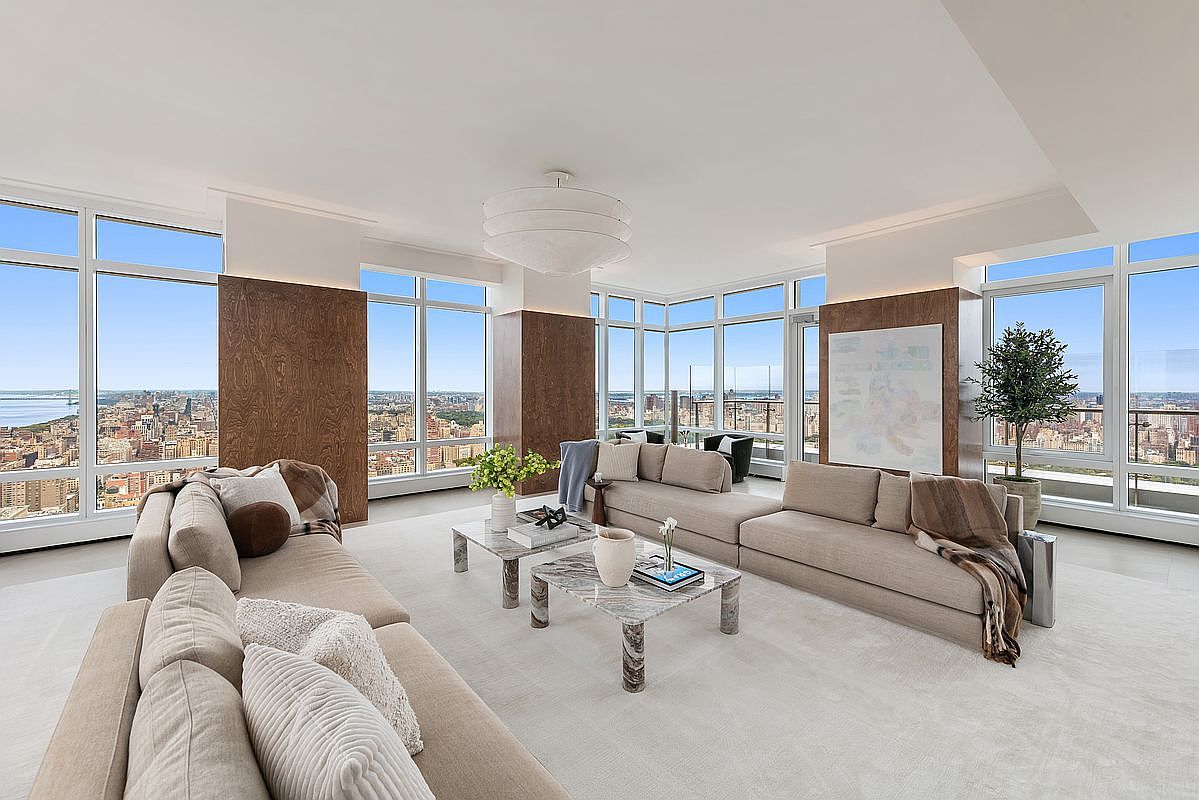 This expansive, high-rise living room features a sophisticated, neutral color palette and floor-to-ceiling windows that offer breathtaking panoramic city views. The space is anchored by two large, plush beige sofas arranged around a pair of elegant marble coffee tables, creating a luxurious and inviting atmosphere. Warm wood-paneled accent walls and a modern, tiered chandelier add depth and architectural interest to this bright, airy, and upscale urban residence.