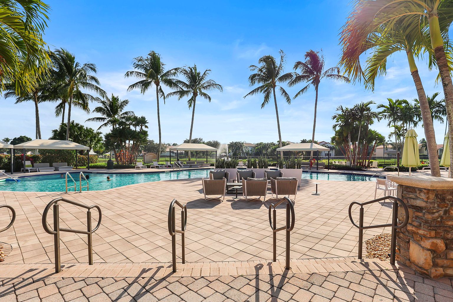 This image showcases a luxurious pool area surrounded by palm trees and lounge seating. The pool is a focal point, complemented by shaded cabanas and a well-maintained patio. The scene evokes a sense of relaxation and resort-style living, perfect for attracting potential buyers seeking leisure and recreation.