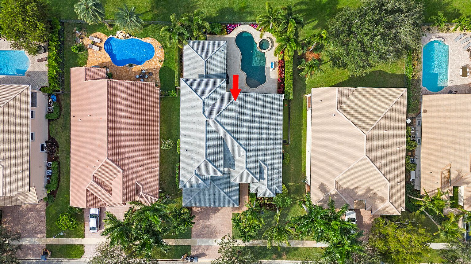This aerial view showcases a well-maintained residential property with a gray tiled roof, surrounded by lush greenery and neighboring houses. A private pool and spa are visible in the backyard, enhancing the property's appeal. The image highlights the property's layout, landscaping, and desirable outdoor amenities.