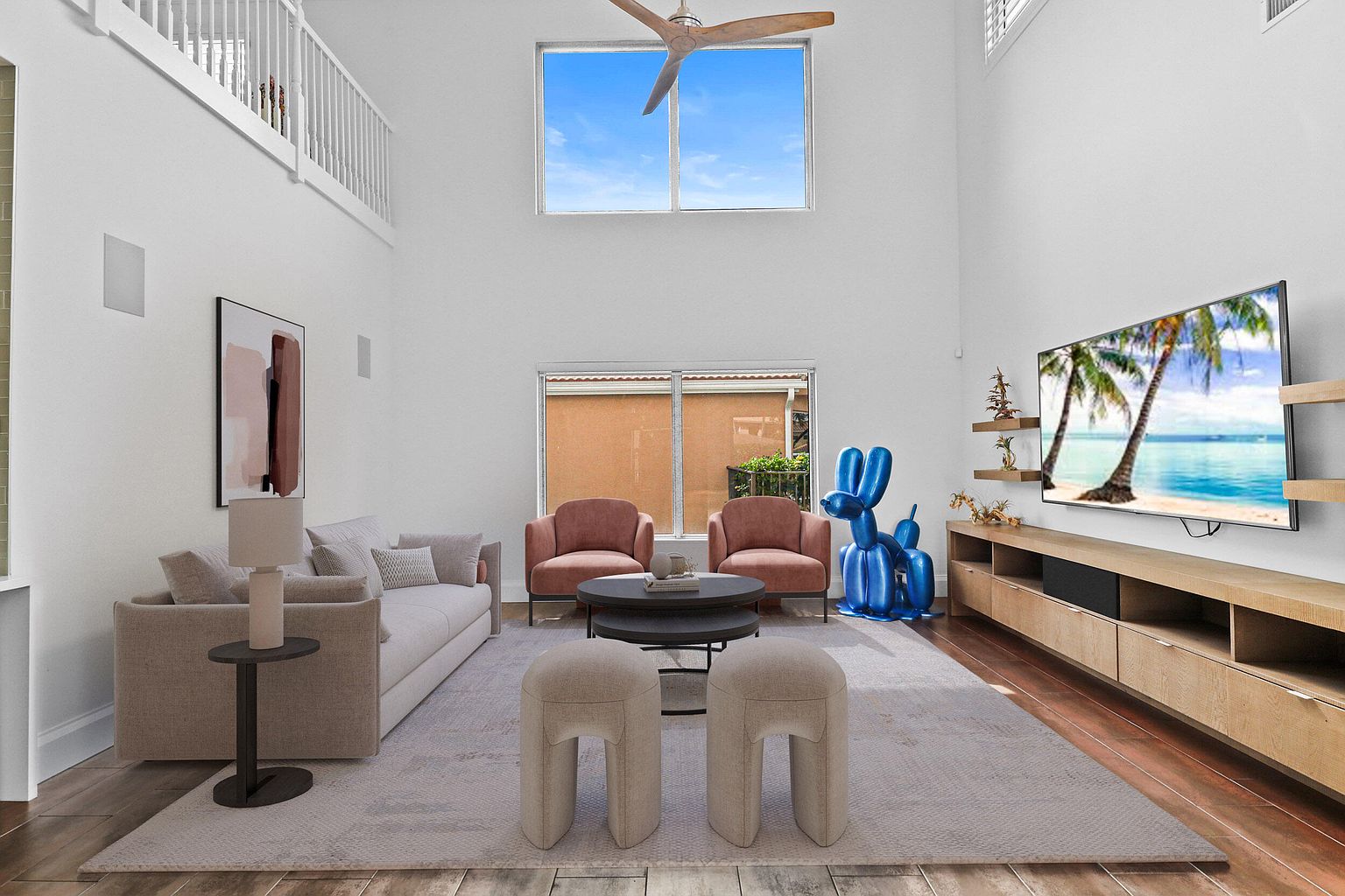 This is a bright and airy living room with a high ceiling and large windows that let in plenty of natural light. The room features a neutral color palette with a beige sofa, two pink armchairs, and a light gray rug. A modern entertainment center with a large television and a blue balloon dog sculpture add a touch of contemporary style.