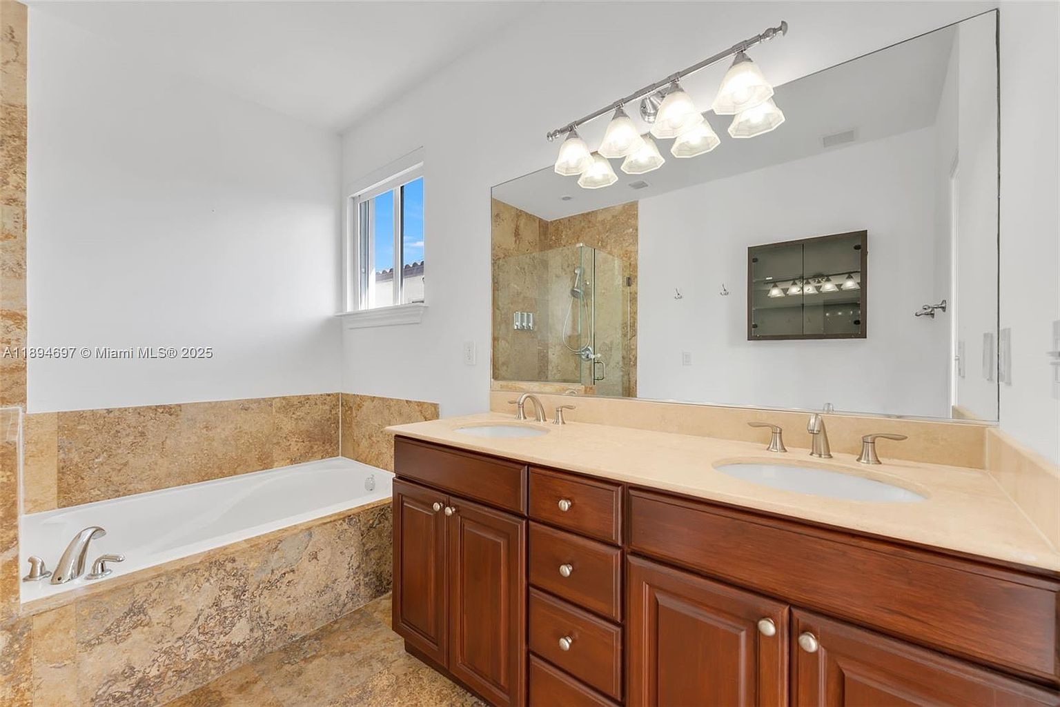 This is a primary bathroom featuring a double vanity with dark wood cabinets and a light-colored countertop. A large mirror reflects the vanity area and a glass-enclosed shower. A bathtub with matching tile surround is visible to the left, creating a cohesive and luxurious space.