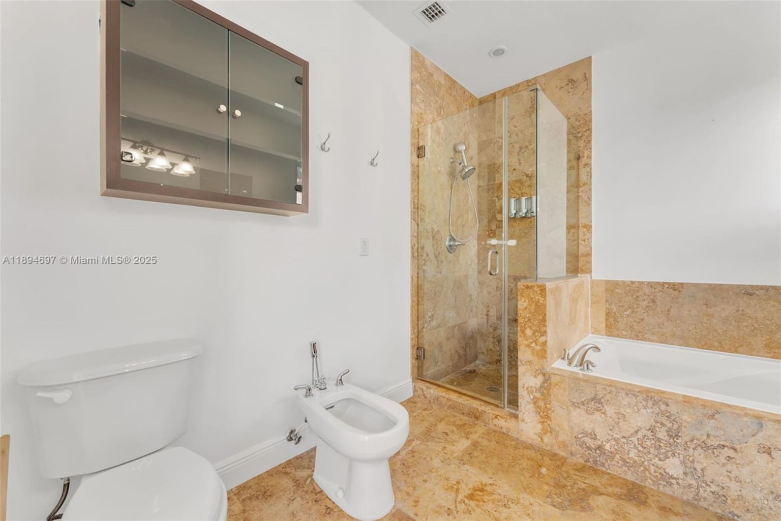 This is a primary bathroom featuring a toilet, bidet, shower, and bathtub. The shower and bathtub are enclosed with glass and marble-like tile, while the walls are painted white. A mirrored cabinet hangs above the toilet, providing storage space.