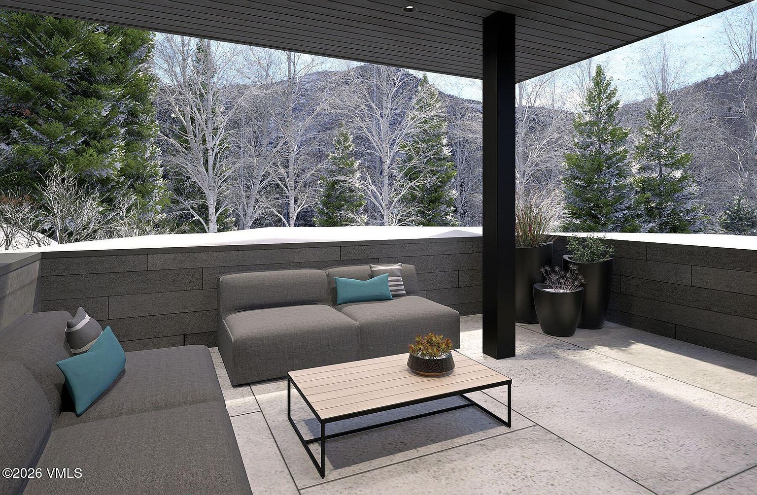 This modern, covered balcony offers a sophisticated outdoor living space with a sleek, minimalist aesthetic. The area is furnished with comfortable grey seating and a low-profile coffee table, set against a backdrop of dark, horizontal-panel walls and a panoramic view of a snow-covered forest and mountains. Potted plants add a touch of greenery to the clean, neutral-toned concrete flooring, creating a serene and inviting atmosphere.