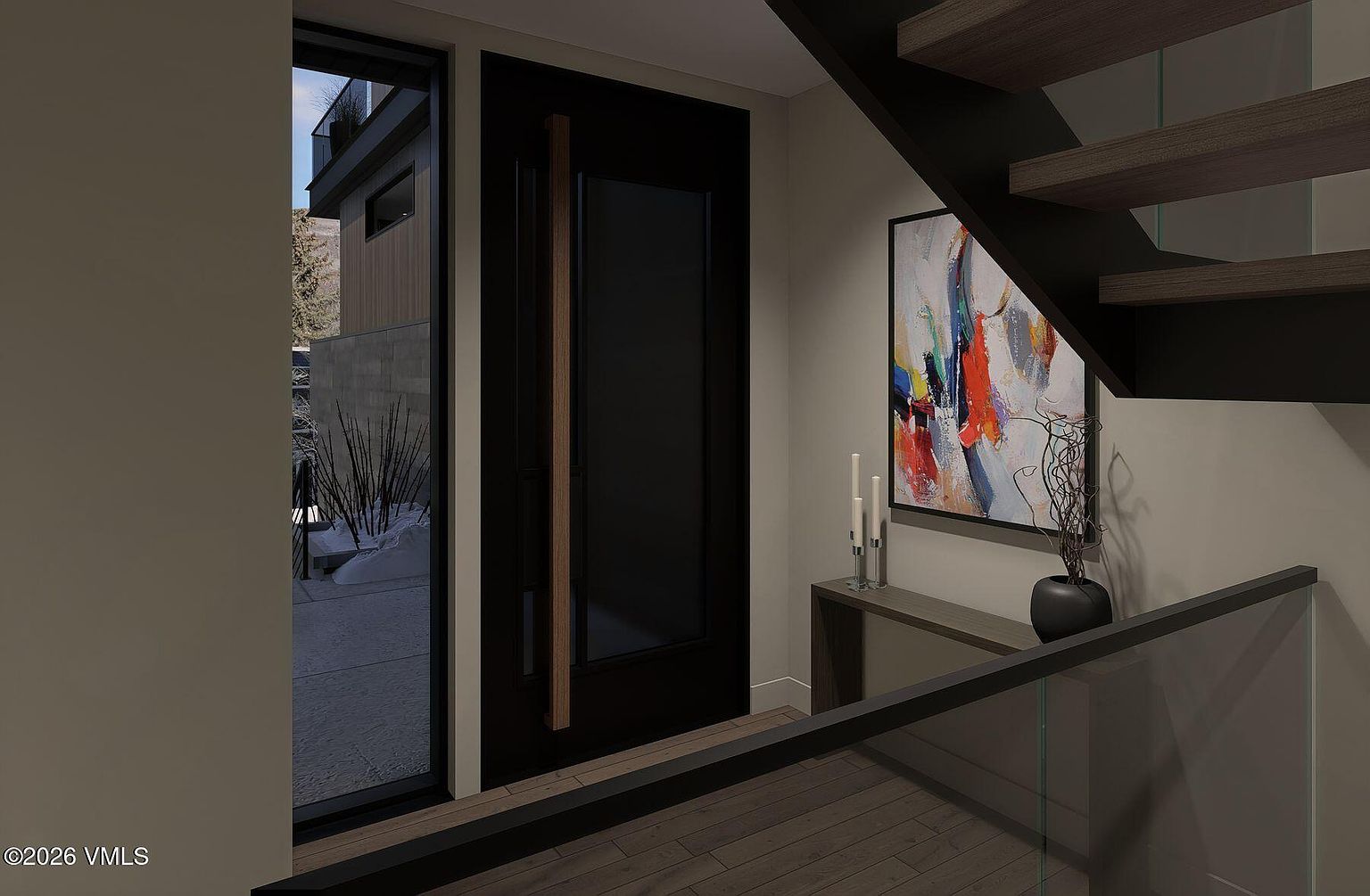 This modern entryway features a striking black front door with a long, vertical wood handle, set against a neutral wall. To the right, a console table holds a decorative vase and candles beneath a vibrant, abstract piece of art, while a glass-railed staircase leads upward. The perspective captures the transition from the interior space to the snowy outdoor view visible through the adjacent tall window.