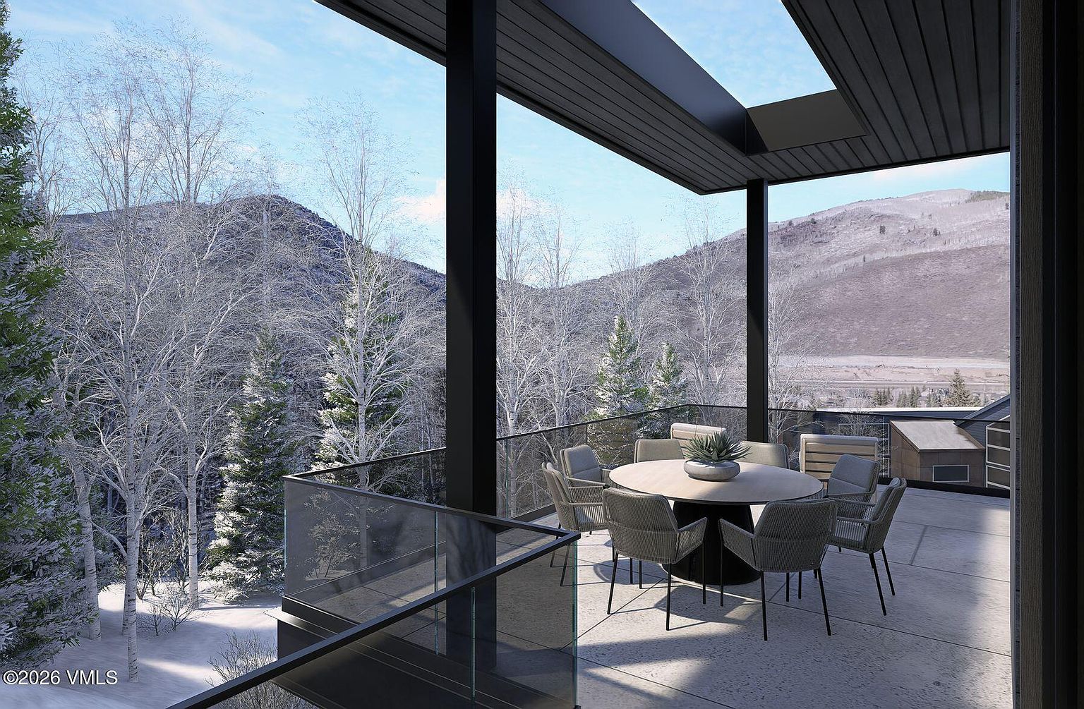 This modern, covered balcony offers a sophisticated outdoor dining space with a circular table and six contemporary chairs. The area features a sleek glass railing that provides an unobstructed, panoramic view of a snow-covered forest and distant mountains. The architectural design includes a dark-toned ceiling and structural supports, creating a sharp contrast against the bright, wintry landscape.