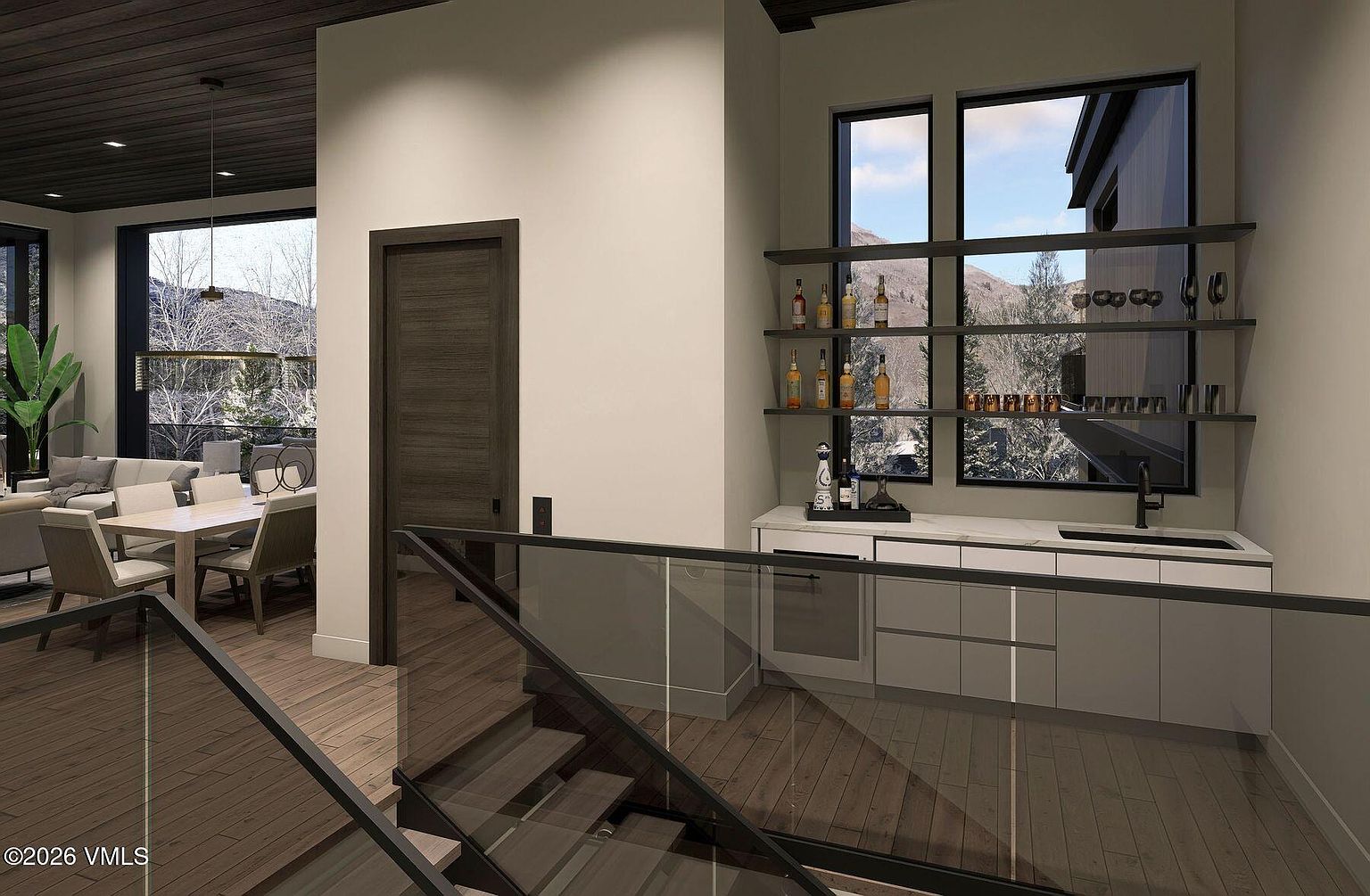 This interior view captures a modern wet bar area adjacent to a staircase with a glass railing. The bar features white cabinetry, a stone countertop, and open shelving stocked with glassware and bottles, set against large windows that provide a view of the outdoors. The space transitions into a dining area, showcasing a contemporary design with clean lines and a neutral color palette.