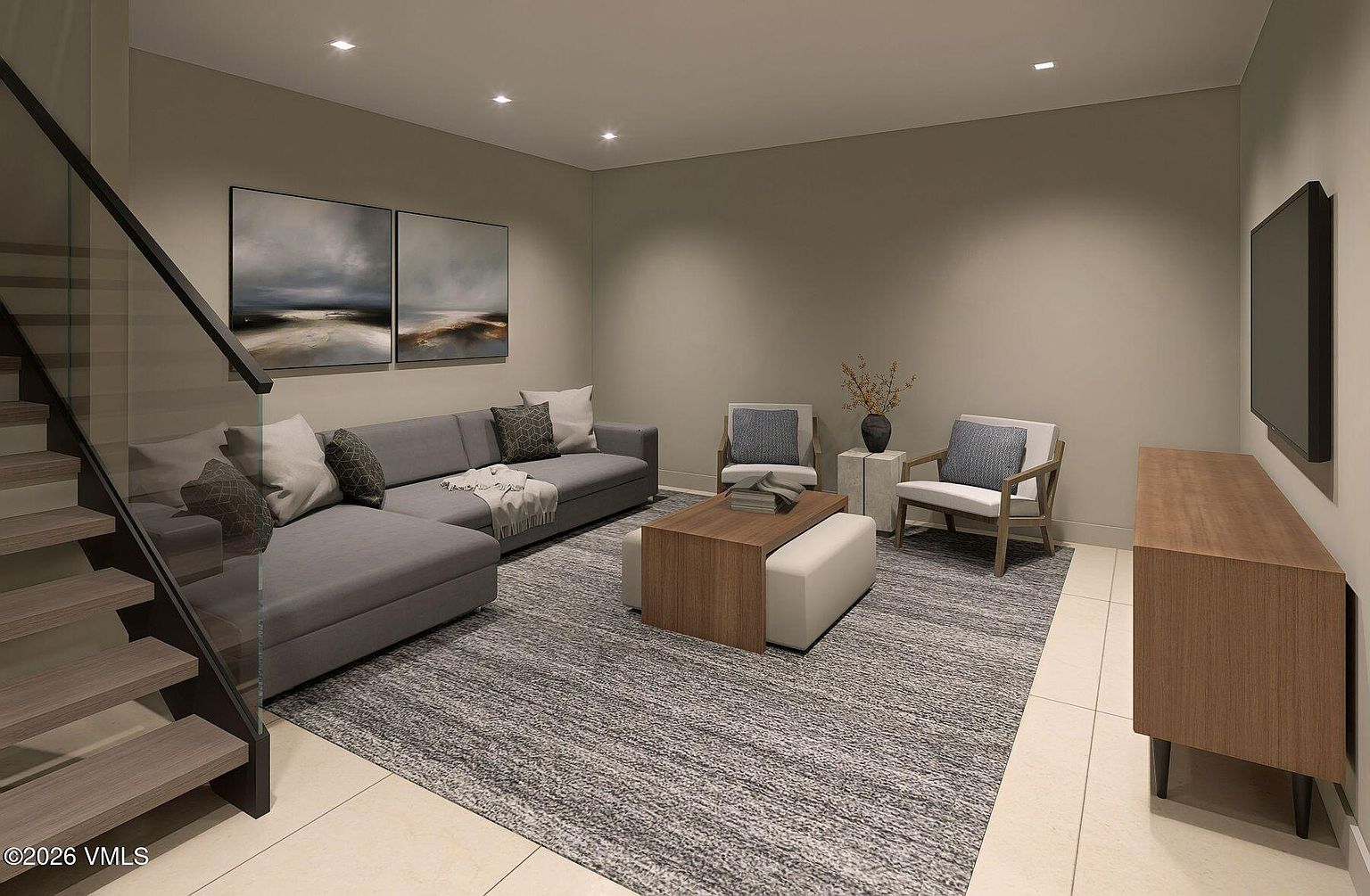 This contemporary living room features a spacious grey sectional sofa accented with patterned throw pillows and a textured rug. A wooden coffee table with a matching ottoman sits in the center, complemented by two armchairs and a sleek media console against the wall. The space is illuminated by recessed lighting and includes a staircase with a glass railing, creating an open and modern atmosphere.