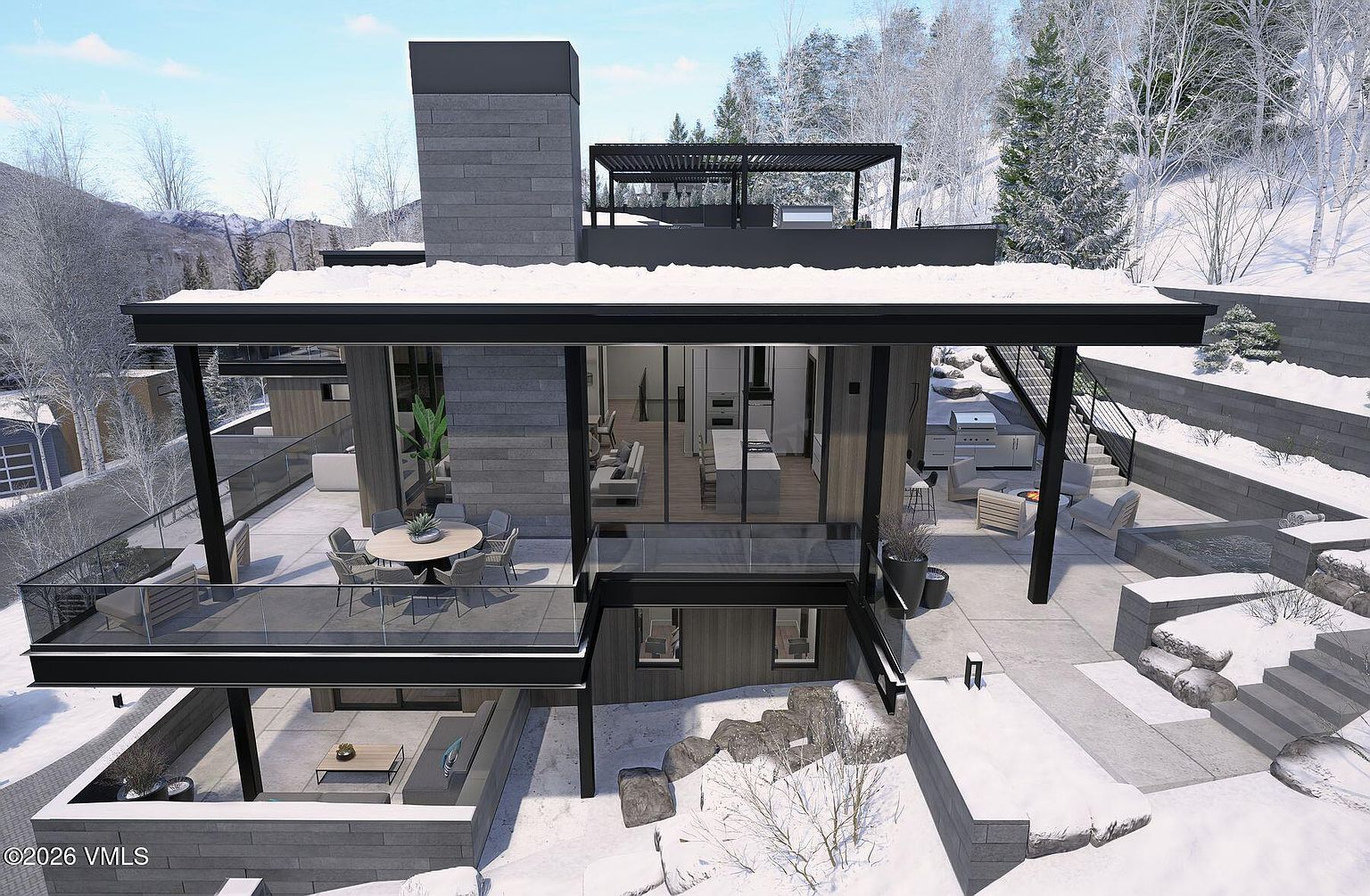 This aerial perspective captures a modern, multi-level mountain residence set against a snowy, forested landscape. The home features a prominent stone-clad chimney breast, expansive glass walls that open to a spacious terrace, and a rooftop deck with a pergola. The exterior design emphasizes clean lines and a seamless transition between indoor living areas and the outdoor patio, which includes a dining space and a fire pit area.