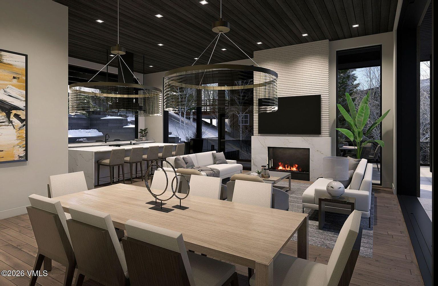 This open-concept living and dining area features a sophisticated, modern aesthetic with a dark wood-paneled ceiling and light wood flooring. The living space is anchored by a fireplace with a tall, light-colored stone surround and a mounted television, while the dining area is defined by a large wooden table and contemporary pendant lighting. Large glass walls provide expansive views of the snowy exterior, creating a seamless connection between the luxurious interior and the natural landscape.