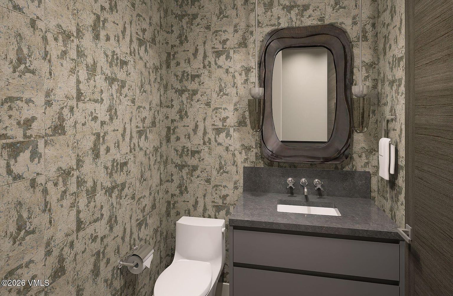 This compact powder room features striking, textured wallpaper with a distressed, metallic-toned pattern that creates a sophisticated atmosphere. A dark, stone-topped vanity with a sleek undermount sink is paired with a unique, organic-shaped mirror and modern pendant lighting. The space is completed by a minimalist white toilet and a wall-mounted towel holder, offering a contemporary and moody aesthetic.