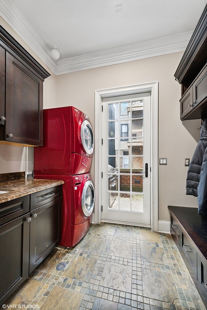 This is a well-appointed laundry room featuring a stacked red washer and dryer set, dark wood cabinetry with granite countertops, and a tiled floor. A glass-paned door provides natural light and a view to the outside. The room appears functional and stylish, offering a blend of practicality and aesthetic appeal.
