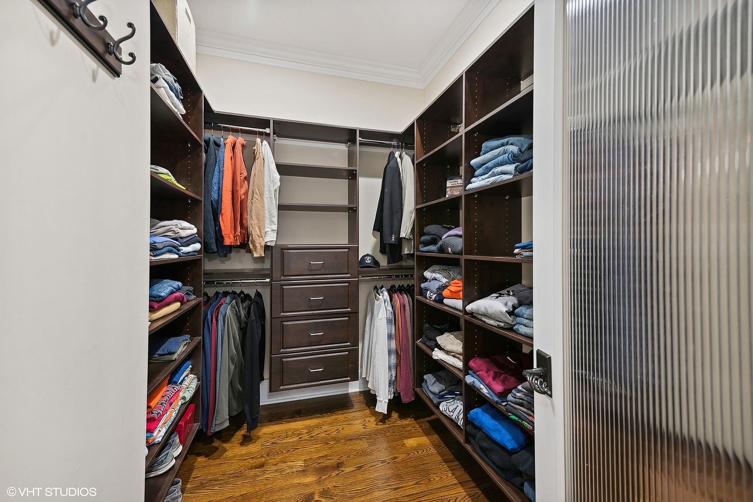 This is a well-organized walk-in closet featuring dark wood shelving and drawers. Clothes are neatly arranged on shelves and hanging rods, maximizing storage space. The hardwood flooring adds a touch of elegance to the space, and the overall impression is one of functionality and style.