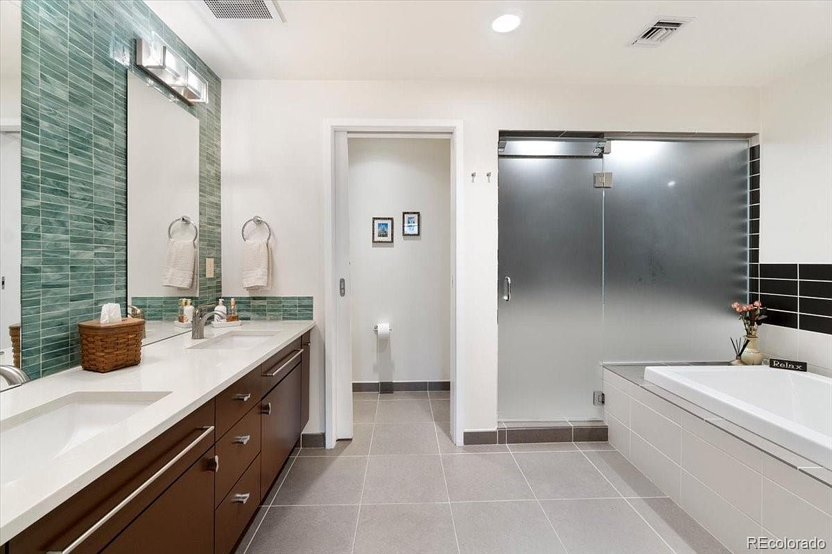 This is a well-lit primary bathroom featuring a double vanity with dark wood cabinets and white countertops. A large mirror is mounted above the vanity, complemented by modern lighting fixtures. The bathroom includes a glass-enclosed shower and a separate bathtub, with neutral-toned tiles covering the floor and walls, creating a clean and contemporary aesthetic.