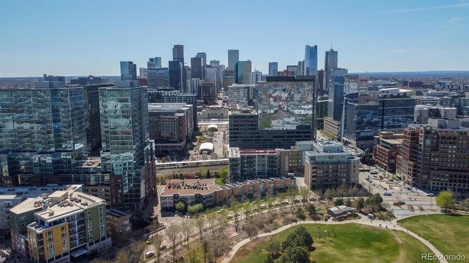 This aerial view showcases a dense urban landscape featuring numerous high-rise buildings and skyscrapers, characteristic of a bustling city center. Green spaces, including a park in the foreground, provide a contrast to the built environment, offering a glimpse of recreational areas. The image provides a comprehensive overview of the area's layout and density, highlighting both residential and commercial properties.
