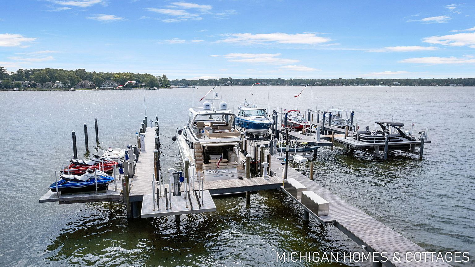 This aerial shot showcases a waterfront property with a substantial dock system. Multiple boats and jet skis are moored at the dock, highlighting the property's direct access to the water. The surrounding landscape includes lush greenery and a clear view of the lake, emphasizing the property's desirable location and recreational opportunities.
