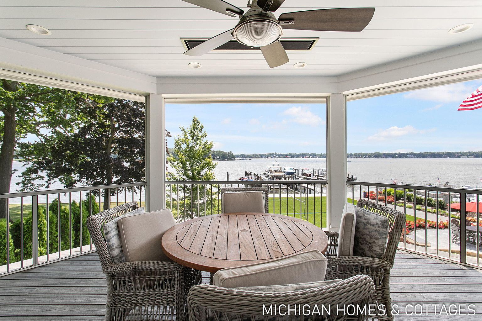 This image showcases a beautifully designed outdoor patio or deck area. The space features a round wooden table surrounded by wicker chairs with comfortable cushions, creating an inviting dining or relaxation area. The patio offers stunning views of the water and surrounding landscape, enhancing the property's appeal.