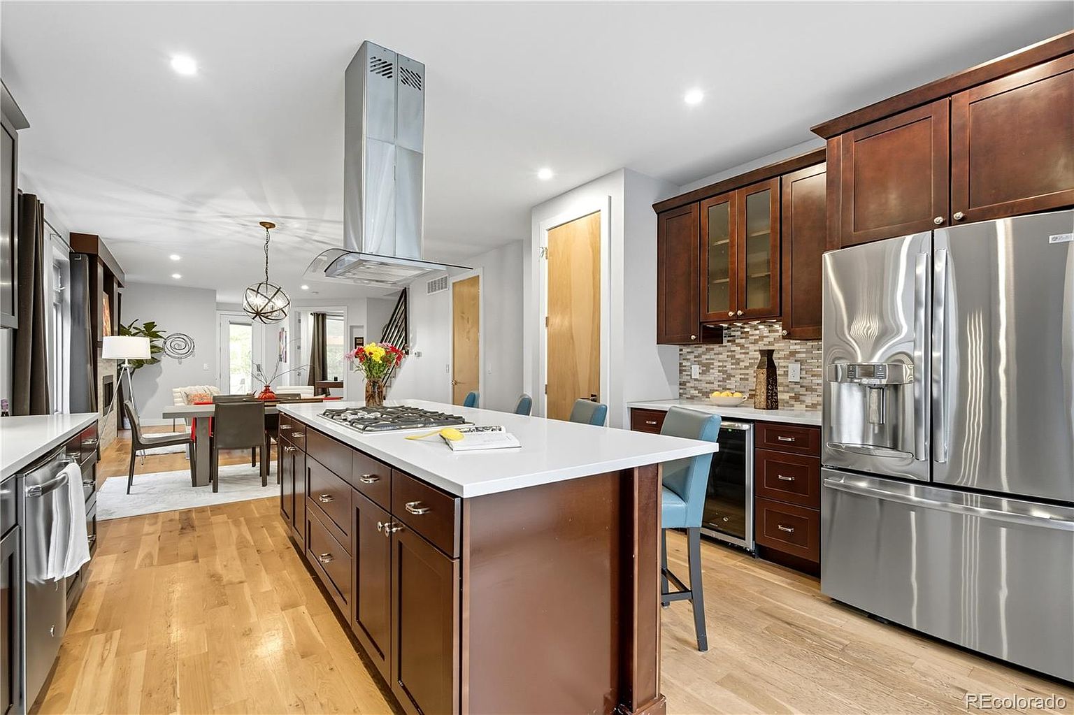 This is a well-lit kitchen featuring dark wood cabinetry, stainless steel appliances, and a large island with a white countertop. The kitchen also includes a dining area with a modern chandelier. The overall impression is one of a modern and functional space.