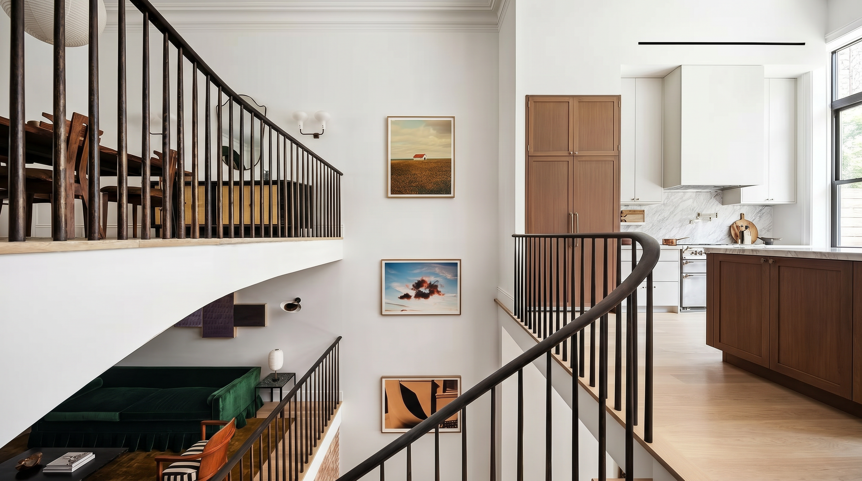 This sophisticated multi-level interior features an open-concept design that connects a living area, dining space, and kitchen through an elegantly curved staircase with dark metal railings. The space highlights clean white walls, natural oak flooring, and wood cabinetry, creating a modern and warm aesthetic. Carefully curated artwork and minimalist lighting add architectural interest, providing an airy and luxurious atmosphere throughout the home.