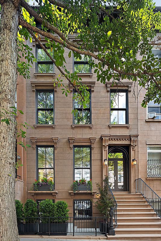 This elegant brownstone townhouse features a classic architectural facade with symmetrical window placement and ornate stone detailing. A grand staircase leads to a sophisticated arched entryway, while lush window boxes and manicured shrubbery add a touch of greenery to the urban setting. The perspective is a straight-on eye-level shot, capturing the timeless charm and refined character of the property.