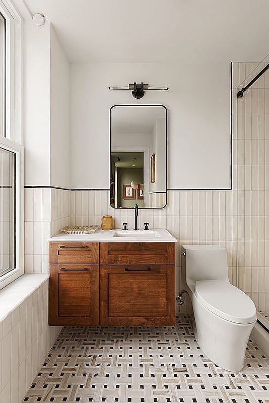 This modern bathroom features a floating wooden vanity with a white countertop and a sleek, rectangular mirror centered above. The walls are adorned with vertical white subway tiles accented by a thin black trim, while the floor showcases a sophisticated basket-weave mosaic pattern. The space is bright and clean, offering a contemporary aesthetic with a focus on high-quality finishes and efficient use of space.