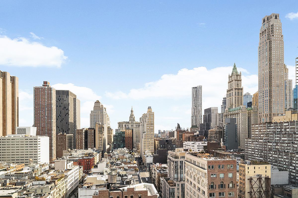 This high-angle aerial view captures a dense, vibrant New York City skyline under a bright, clear blue sky. The composition showcases a mix of historic and modern architecture, including iconic skyscrapers and classic brick buildings with rooftop water towers. The perspective provides a sweeping, cinematic sense of urban scale and metropolitan life.