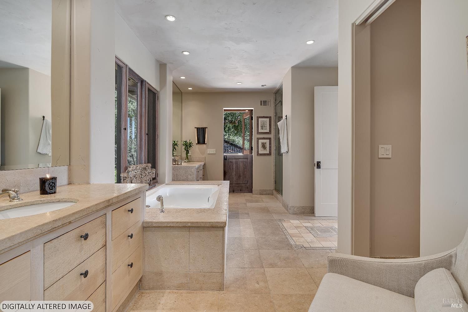 This spacious primary bathroom features a neutral, earthy color palette with stone tile flooring and matching vanity countertops. The room includes a deep soaking tub, a double vanity, and a Dutch-style door leading to an outdoor area, creating a bright and airy atmosphere. The perspective is from the entrance, showcasing the clean lines and high-end finishes that define this luxurious retreat.