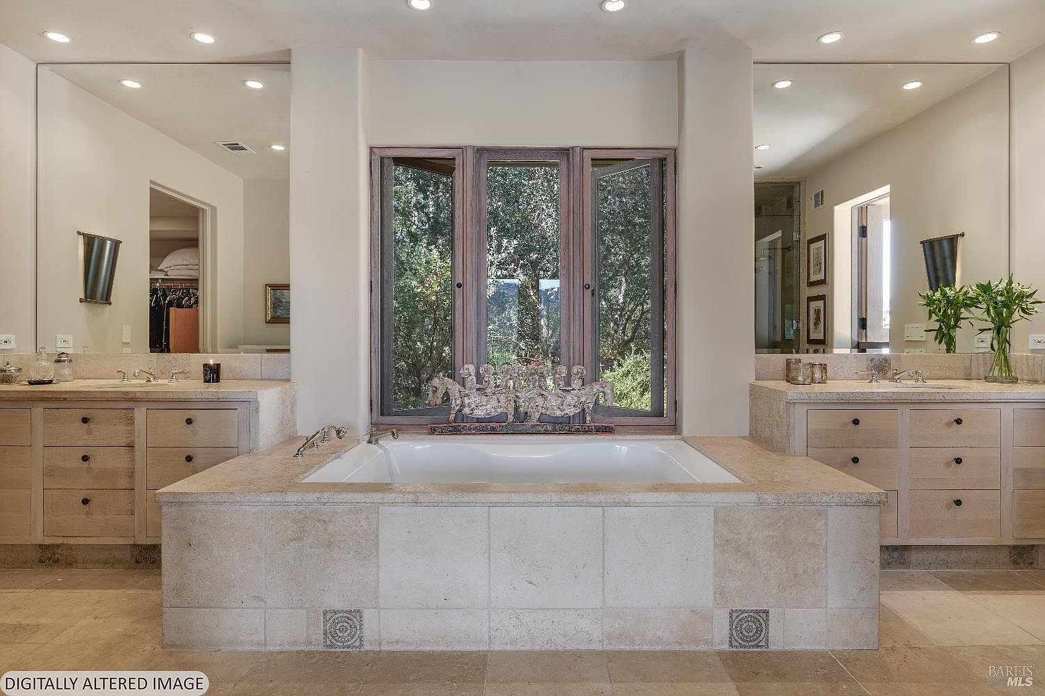 This luxurious primary bathroom features a central soaking tub encased in light-toned stone, flanked by dual vanities with matching cabinetry and large mirrors. A large, multi-pane window behind the tub provides a serene view of the surrounding trees, while recessed lighting creates a warm and inviting atmosphere. The space is designed with a neutral color palette and high-end finishes, offering a spa-like retreat.