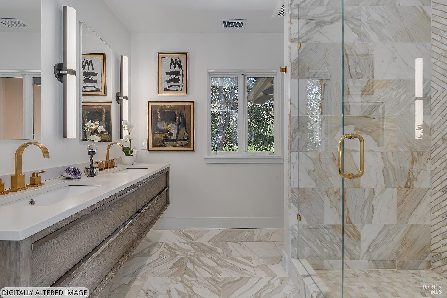 This luxurious primary bathroom features a sleek, floating wood-toned double vanity topped with white quartz and accented by modern gold fixtures. A spacious walk-in shower with floor-to-ceiling marble tile and a glass door serves as a focal point, complemented by elegant framed artwork on the wall. The room is bright and airy, with large windows and sophisticated lighting that creates a high-end, spa-like atmosphere.