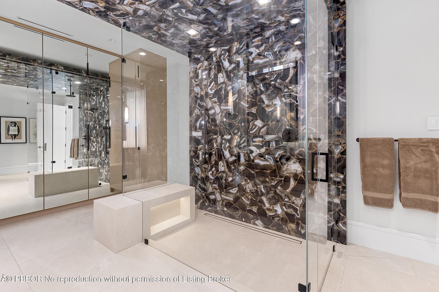 This is a luxurious primary bathroom featuring a glass-enclosed shower with unique stone slab walls and ceiling, creating a dramatic and high-end aesthetic. A modern bench with integrated lighting sits adjacent to the shower, and a large mirror reflects the space, enhancing the sense of openness. The overall impression is one of opulence and contemporary design.
