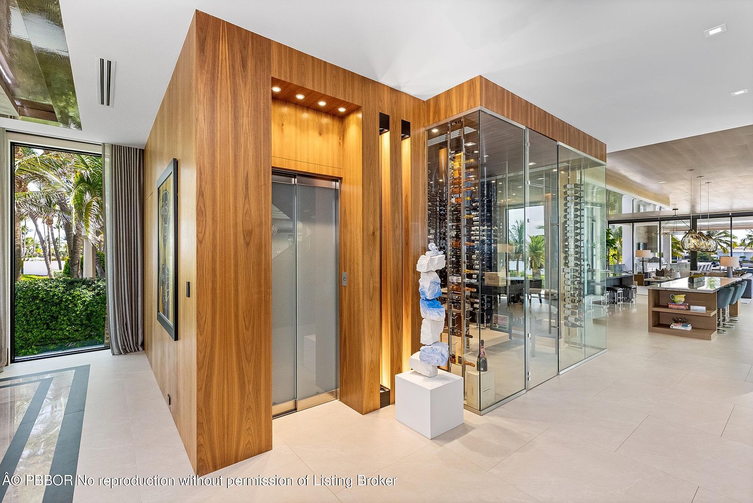 This interior shot showcases a modern hallway featuring a wood-paneled elevator and a glass-enclosed wine cellar. The hallway is brightly lit with recessed lighting and natural light from a nearby window, highlighting the clean lines and luxurious finishes. The perspective is from a medium angle, emphasizing the depth and architectural details of the space.